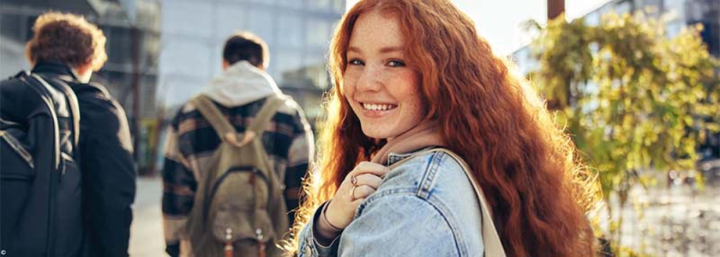 Foto: Teenager Mädchen läuft mit einer Gruppe in die Schule und schaut über die Schulter zurück in die Kamera.