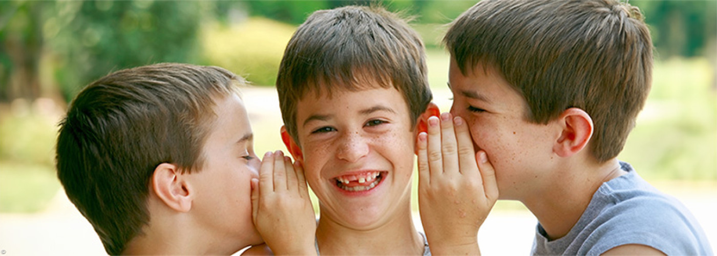 Foto: zwei Jungen flüstern einem anderen Jungen etwas ins Ohr