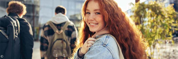 Foto: Teenager Mädchen läuft mit einer Gruppe in die Schule und schaut über die Schulter zurück in die Kamera.